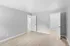 Bright and spacious bedroom with light wood flooring, two open doors, and neutral gray walls.