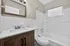 Modern bathroom with sleek white tiles, a stylish wooden vanity, and a bright window providing natural light.
