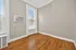 Bright, cozy room with hardwood floors, large window, and in-wall air conditioning unit.
