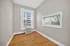 Bright and airy room with hardwood floors, large windows offering city and treetop views, ideal for a home office or cozy retreat.
