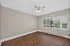 Bright, empty room with elegant wood flooring and a large window offering natural light, featuring a ceiling fan for optimal comfort.