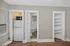 Compact kitchenette area with a sleek white refrigerator and microwave, adjacent to a cozy living space with wood flooring and built-in shelving.