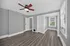 Bright and spacious room with elegant gray walls, rich wood flooring, and a classic ceiling fan, complemented by large windows for natural light.