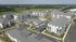 Aerial view of a modern apartment complex with multiple buildings, a central pool area, ample parking, and scenic green surroundings.