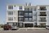 Modern apartment complex exterior with stylish facade, featuring multiple floors, balconies, and ample parking in a serene setting.