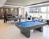 Modern lounge space with billiards and ping pong tables, large windows overlooking a vibrant outdoor area.