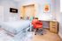 Modern bedroom with a comfortable Murphy bed, vibrant red office chair, and sleek wooden desk, perfect for a stylish and functional living space.