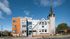 Contemporary apartment building with striking modern design, featuring a blend of orange and gray facade, large windows, and a distinctive spire, set against a clear blue sky.