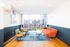 Bright and inviting lounge area with stylish orange sofa, chic green armchairs, and modern decor, offering a vibrant view through large floor-to-ceiling windows.