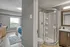 Modern apartment featuring a bright bedroom with large window and cozy decor, adjacent to a sleek bathroom with a glass-enclosed shower and elegant vanity.