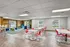 Modern communal lounge area featuring vibrant red chairs, sleek white tables, and cozy seating with rustic wood accents and large bright windows.