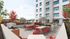 Modern outdoor patio with vibrant red chairs and tables, equipped with a sleek BBQ grill, set against a backdrop of a stylish apartment building and lush, colorful landscaping.