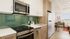 Bright, stylish kitchen with modern appliances, green tile backsplash, and cozy workspace in a sunlit corner.