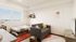 Bright and cozy bedroom with a scenic view, featuring a comfy bed, stylish gray sofa, and modern decor with shelves and artwork.
