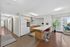 Modern apartment interior featuring a sleek kitchen with white countertops, stylish bar stools, and a cozy living area with large windows and lush plants.
