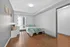 Bright and airy bedroom with modern decor, featuring sleek hardwood flooring, a cozy bed with soft green accents, and natural light pouring in from a large window.