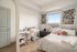Inviting bedroom with modern decor, featuring bright white walls, cozy bed with plush pillows, and a charming study area next to a large window offering natural light.