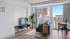 Modern living room with stylish decor, featuring a cozy gray sofa, flat-screen TV, and large windows offering ample natural light.