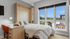 Bright bedroom with large windows, cozy bed, and stylish wooden desk; perfect for a serene home office setup.