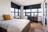 Bright, modern bedroom with city views, featuring sleek furniture and a cozy work space.