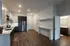 Modern apartment kitchen with sleek cabinetry, stainless steel appliances, and beautiful wood flooring, leading to a bright bathroom area.