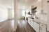 Modern kitchen with sleek white cabinetry and stainless steel appliances, opening into a bright, spacious room with elegant hardwood floors.