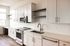 Bright and modern kitchen featuring sleek white cabinets, stainless steel appliances, and elegant wood flooring, perfectly illuminated by large windows.