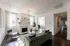 Elegant living room featuring a chic green sofa, modern light fixture, and a cozy fireplace, with ample natural light streaming through large windows.