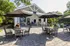 Inviting outdoor seating area with shaded tables and a charming building, surrounded by lush greenery, ideal for relaxation.