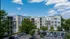 Modern apartment residences with crisp architecture, lush greenery, and ample parking under a clear blue sky.