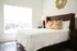 Bright and stylish bedroom featuring a plush bed with a tufted headboard, vibrant patterned pillows, and elegant decor beneath a sunburst mirror.