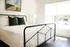 Bright and inviting bedroom showcasing a modern black metal bed frame, elegant white linens, and plush green pillows, complemented by natural light streaming through large windows.