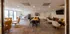 Spacious and elegant meeting room with modern decor, featuring a long wooden table, stylish chairs, and a cozy seating area. Large windows provide ample natural light, enhancing the warm atmosphere.