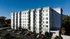 Modern seven-story apartment building with elegant balconies and ample parking, set against a clear blue sky.