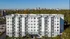 Modern apartment building with elegant balconies and ample parking, set against a stunning cityscape backdrop and lush greenery under a clear blue sky.