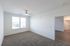 Bright and airy bedroom with plush carpet, large windows, and a ceiling fan, leading to a stylish and modern living room