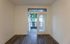 Bright and inviting room with elegant hardwood floors, featuring a glass door opening to a cozy balcony with a lush garden view.