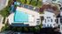 Aerial view of a luxurious residential complex featuring a sparkling swimming pool, sun loungers, and a spacious patio area with lush landscaping.