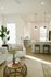 Bright and inviting living space with modern decor, featuring a cozy armchair, stylish rattan table, and sleek open kitchen with pendant lighting.