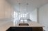 Modern kitchen with sleek quartz countertops, stylish pendant lighting, and an open-plan view into a bright living space with large windows.