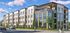 Elegant modern apartment building with large windows and a stylish rooftop terrace on a sunny day, showcasing vibrant landscaping and street activity.