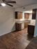 Inviting apartment kitchen with dark wood cabinets, modern appliances, and elegant lighting, complemented by warm wooden flooring.