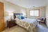 Inviting bedroom with elegant decor, featuring a plush bed with patterned bedding, modern nightstand, stylish chair, and large window providing ample natural light.
