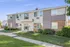 Modern two-story apartment building with a well-maintained lawn and clear blue sky.