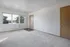 Spacious room with large window, fresh carpet, and wooden door, offering ample natural light.