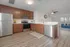 Modern kitchen with sleek stainless steel appliances, wood cabinetry, and an open layout leading to a bright living area with a cozy blue sofa and stylish ceiling fan.