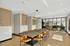 Modern dining area with stylish wooden table, sleek pendant lighting, and vibrant orange chairs, complemented by open glass partitions leading to a cozy lounge space.