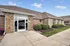 Charming brick building with large windows and well-manicured landscaping, featuring shrubs and vibrant flowers at the entrance.