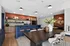 Chic modern kitchen and dining area with elegant decor, featuring a bold blue island, stylish bar stools, and a large dining table with vase centerpiece.