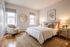 Bright and cozy bedroom with a stylish beige theme, featuring a comfortable bed with fluffy pillows, a chic armchair by the window, and warm lighting from elegant lamps.